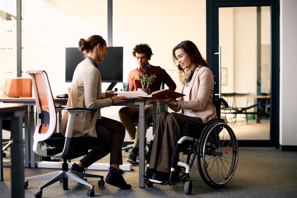 Happy businesswoman with disability and her female colleague cooperating while working on paperwork in the office