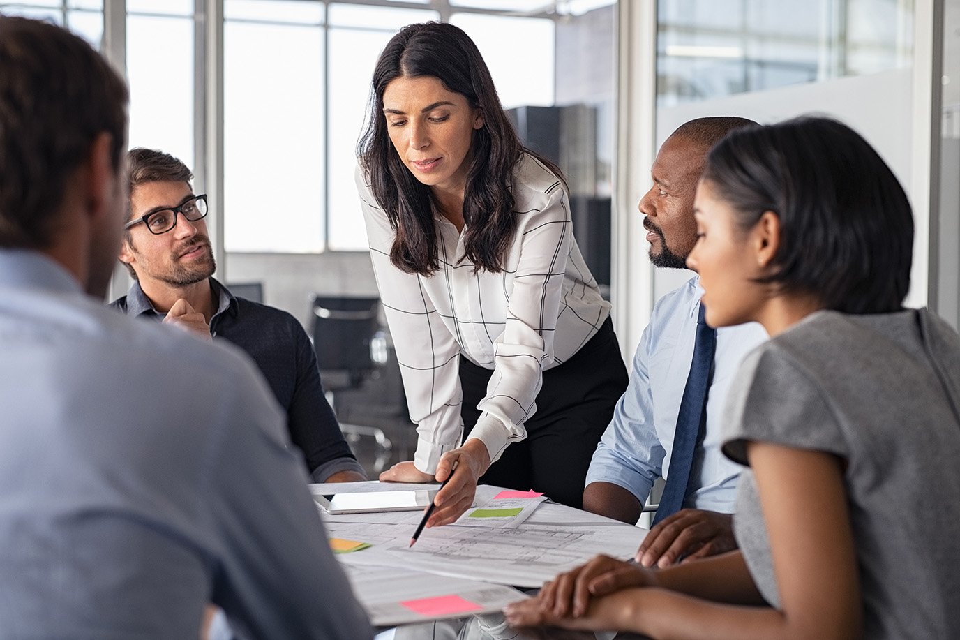 Team of multiethnic architects working on construction plans in meeting room. Engineers and designers discussing project in office. Businesswoman with business team in conference room working on blueprint.